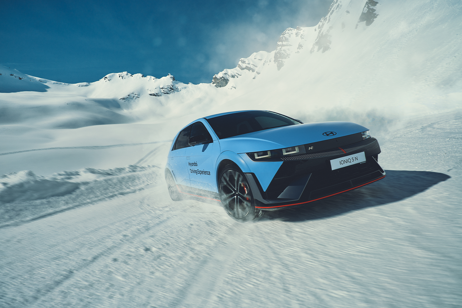A Hyundai IONIQ 5 N electric car drifting through snow on a mountain, kicking up powder as it demonstrates its handling capabilities during the Hyundai Driving Experience.