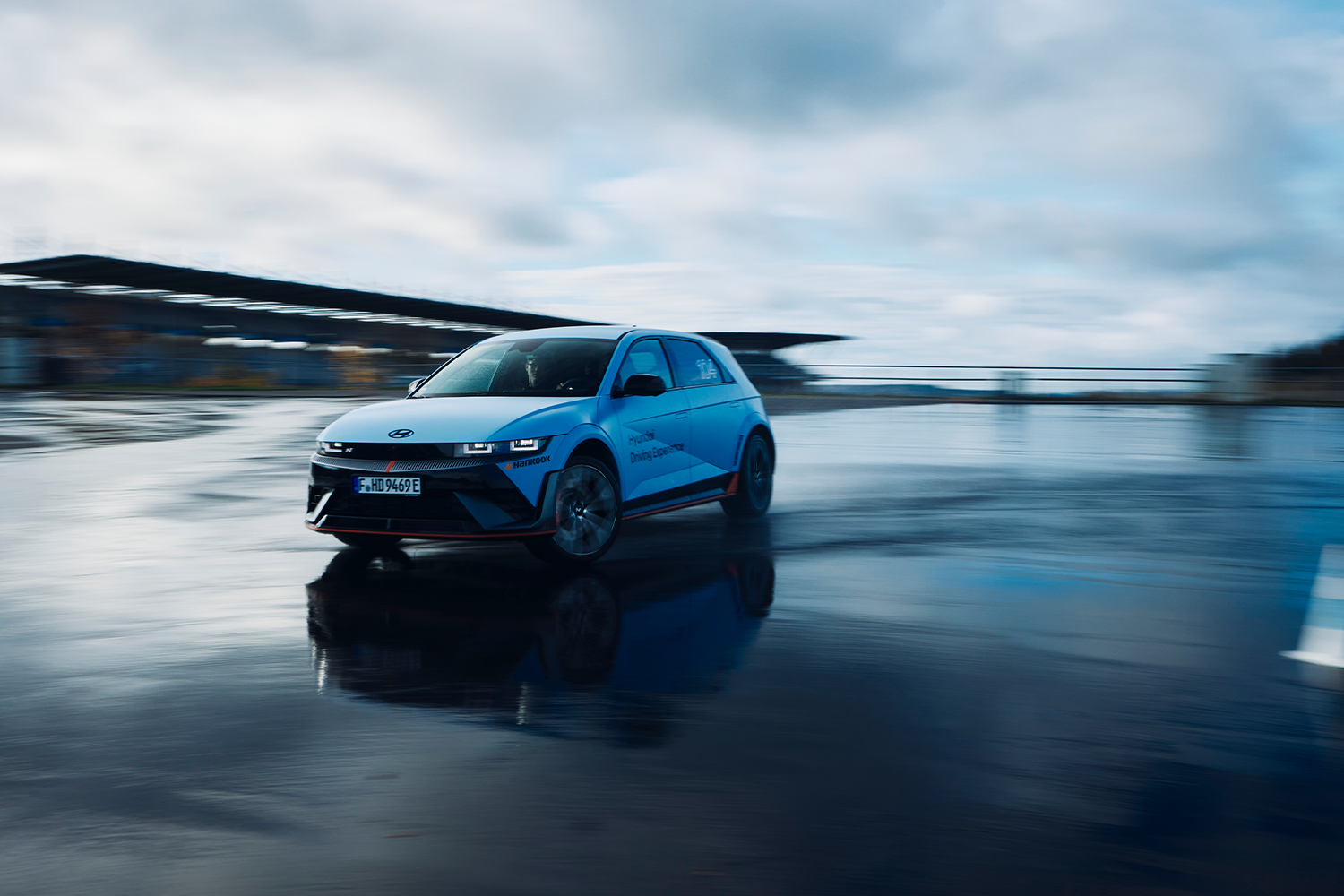 Hyundai IONIQ 5 N driving on a wet track during the Hyundai Driving Experience, with motion blur and reflections on the slick surface.
