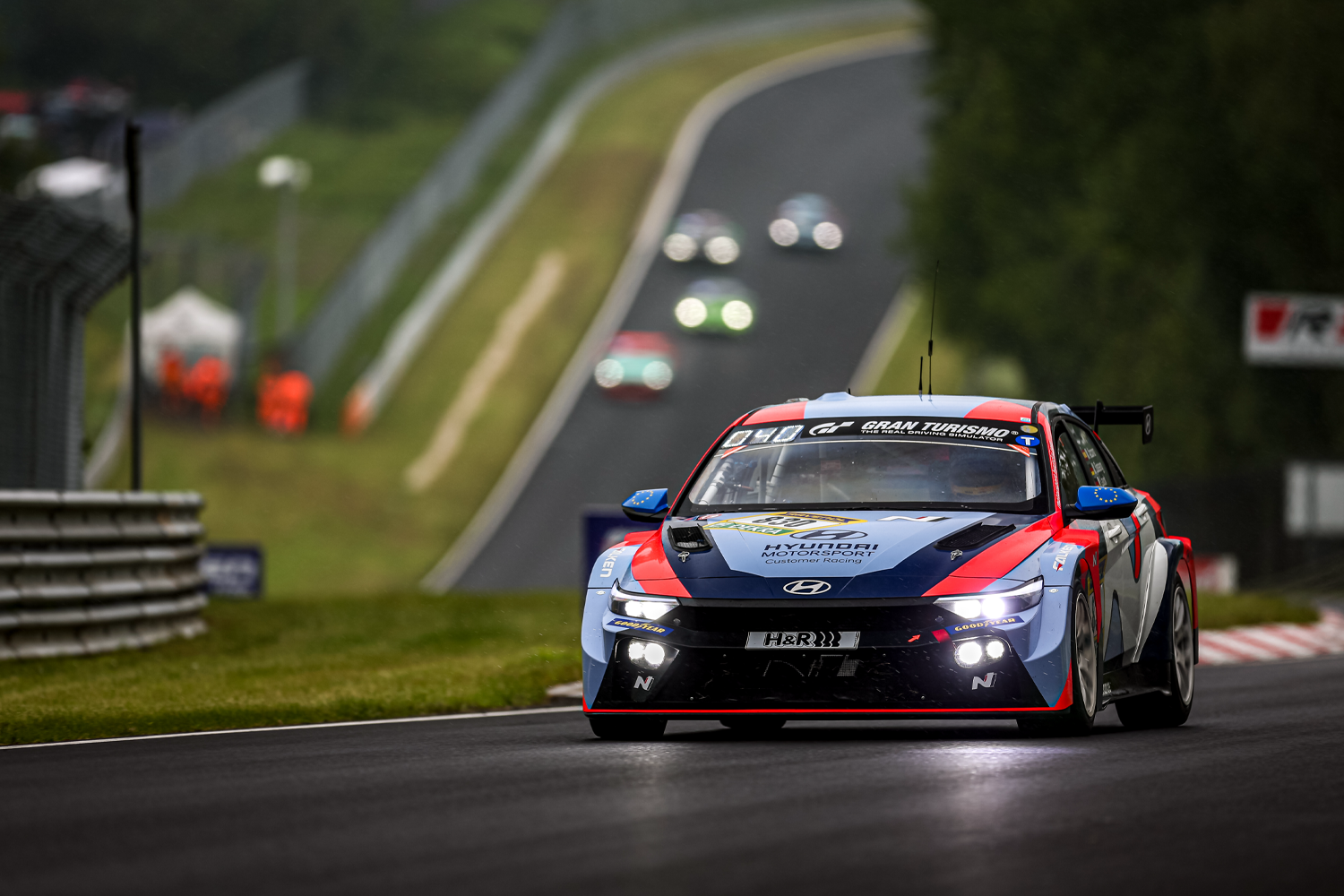 Hyundai Motorsport-Rennwagen auf der Nürburgring-Strecke, der sein auffälliges Design und seine Leistung unter Wettbewerbsbedingungen zeigt, mit unscharfen Hintergrundelementen.
